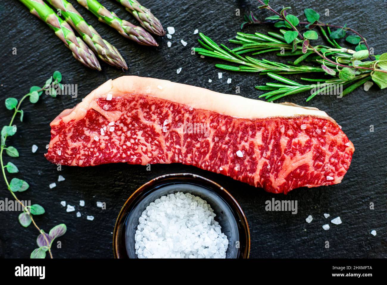 Marmoriertes japanisches Wagyu-Streifensteak mit grünen Kräutern und Spargel Stockfoto