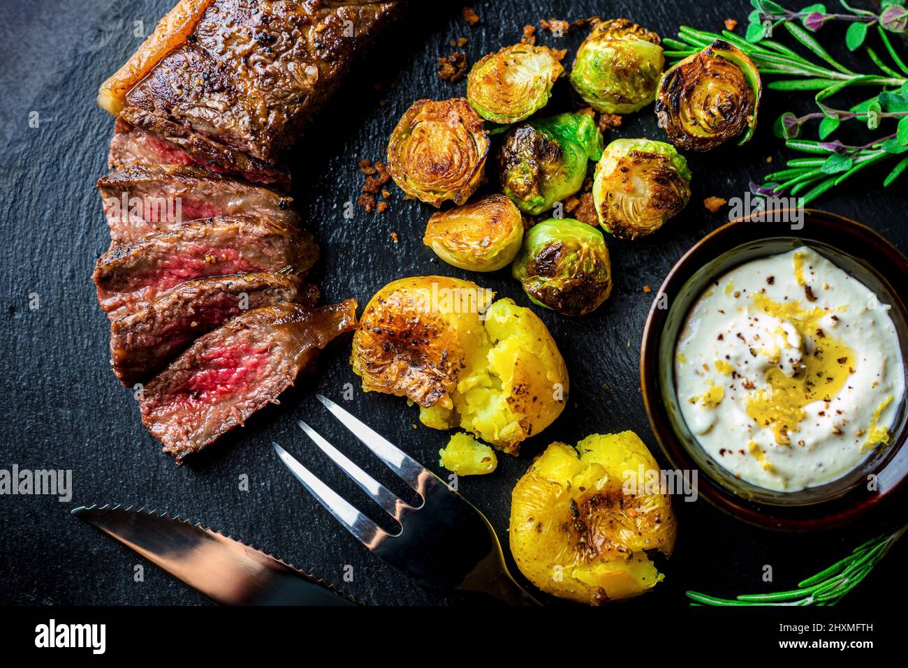 Schneiden Sie das mittelseltene Wagyu-Streifensteak mit gerösteten Tomaten und rosenkohl Stockfoto