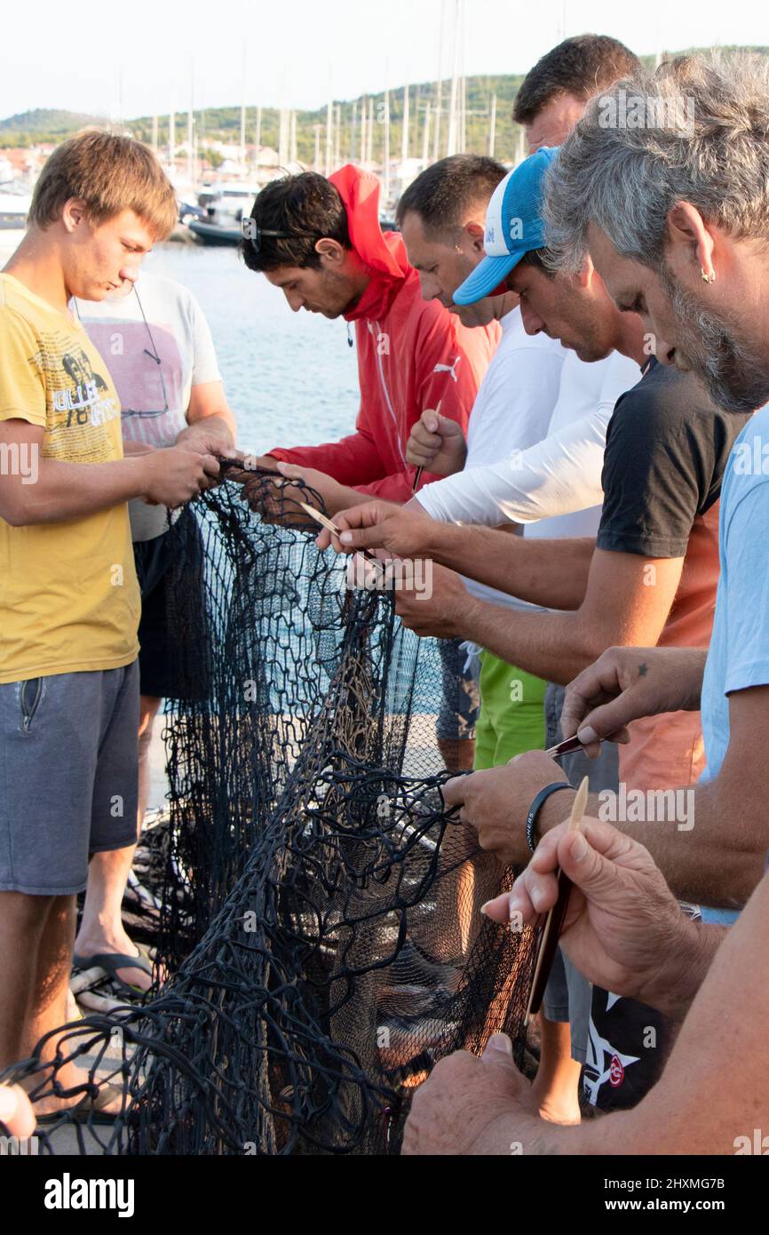 Tribunj, Kroatien - 23. August 2021: Gruppe von Fischern, die das Fischernetz reparieren, Nahaufnahme Stockfoto