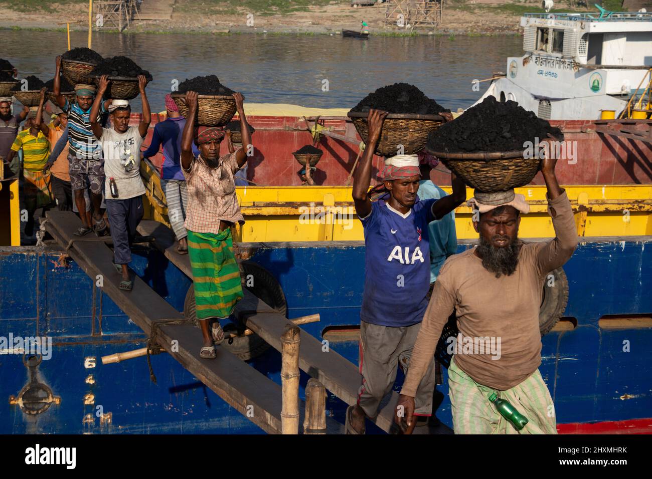 Dhaka, Dhaka, Bangladesch. 13. März 2022. Arbeiter transportieren Körbe voller Kohle auf ihren Köpfen, während sie Kohle von einem Frachtschiff in Dhaka, Bangladesch, entladen. Etwa 3,0 Prozent der Energie des Landes stammt derzeit aus Kohle. An diesen Häfen werden kohlebeladene Güter aus Indien, Indonesien und Afrika verladen. Tagelöhner verdienen rund $1 für je 30 Körbe Kohle, die vom Schiff entladen werden. Am frühen Morgen beginnen die Arbeiter, Kohlen bis zum Sonnenuntergang zu entladen, sie verdienen $5 bis $7 Dollar pro Tag. Es gibt keine speziellen Schuhe an ihren Füßen und keine Handschuhe in ihren Händen, um Kohle von Frachtschiffen zu entladen. Moreo Stockfoto