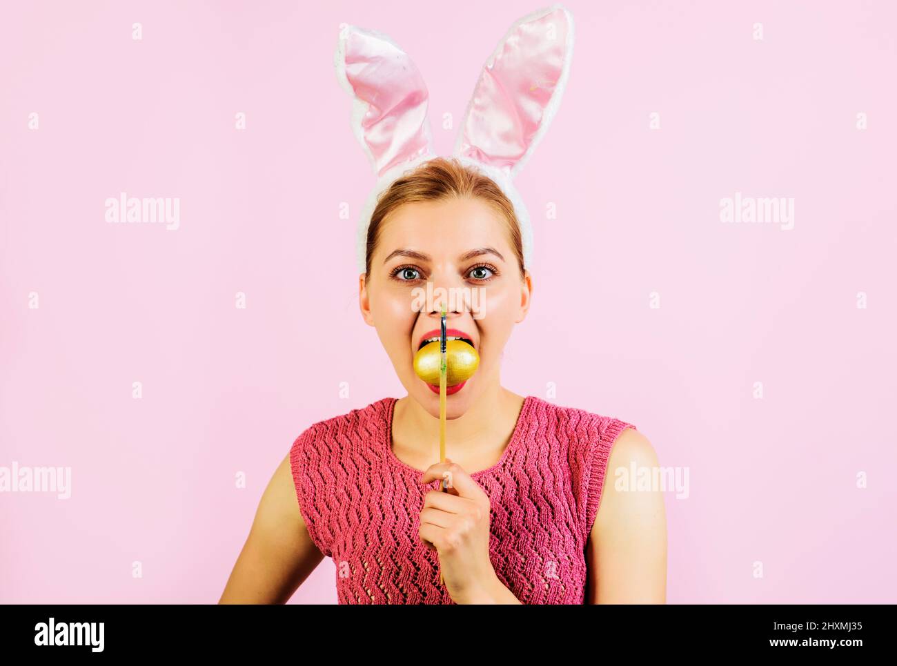 Ostereier-Ideen. Eiersuche. Frau in Hasenohren mit bemaltem Ei im Mund. Frühlingsferien. Stockfoto