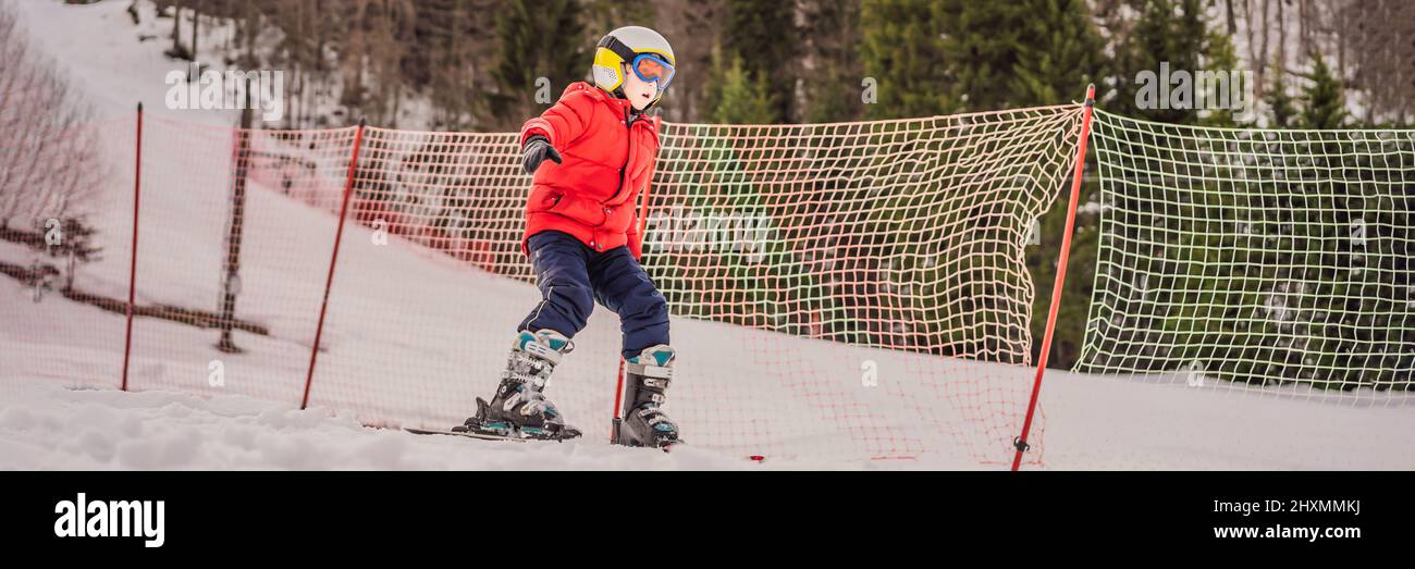 BANNER, LANGFORMAT Kinderskifahren in den Bergen. Aktives Kleinkind mit Schutzhelm, Schutzbrille und Stöcken. Skirennen für kleine Kinder. Wintersport für Stockfoto