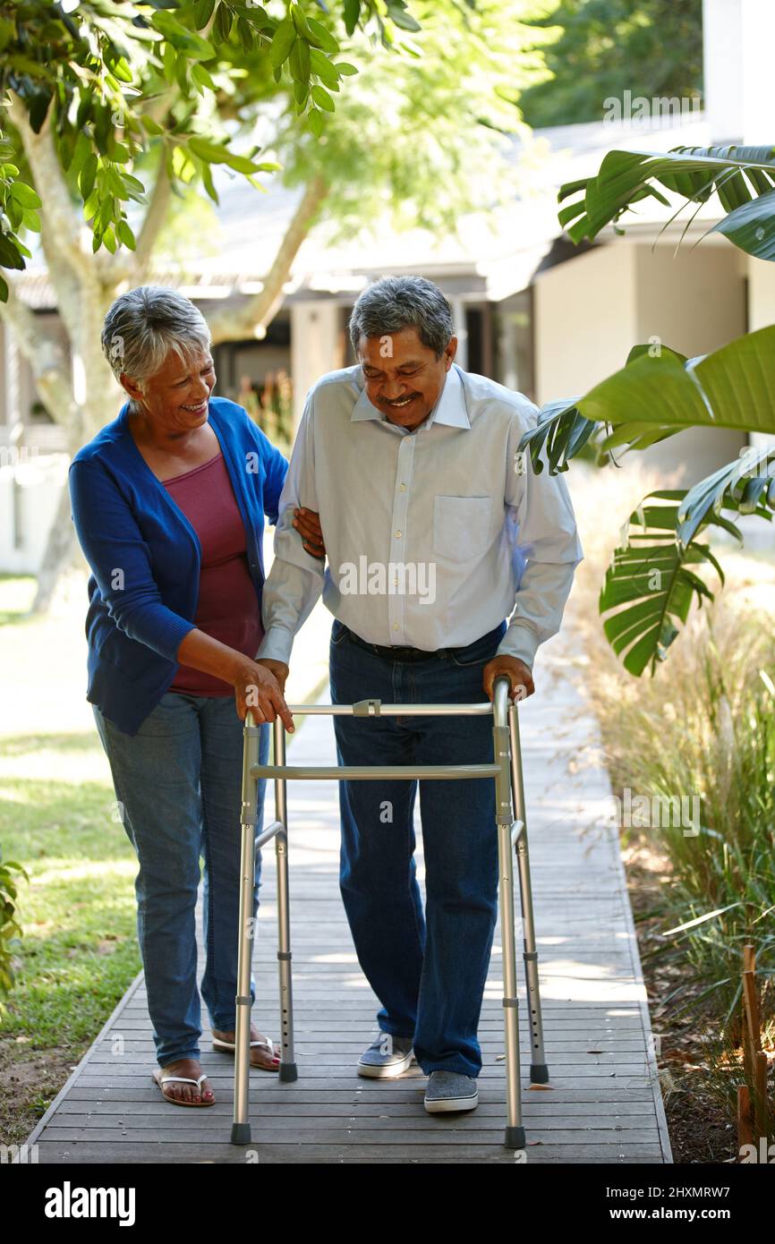 Selbst der kleinste Schritt ist immer noch ein Fortschritt. Aufnahme einer älteren Frau, die ihrem Mann bei der Anpassung an seinen neuen Wanderer hilft. Stockfoto