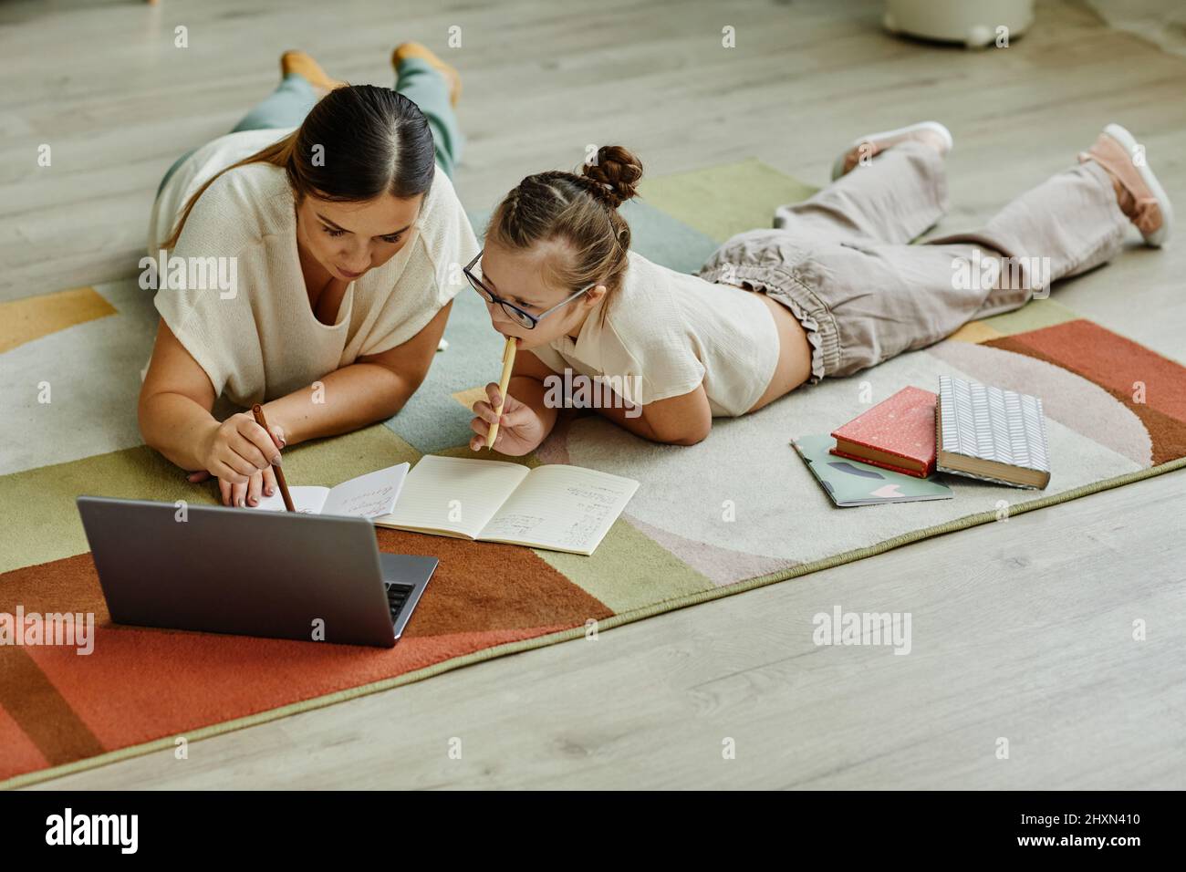 Mutter hilft Mädchen mit Down-Syndrom zu Hause studieren, während sie auf dem Boden zusammen liegen, nicht traditionelle Bildung Stockfoto