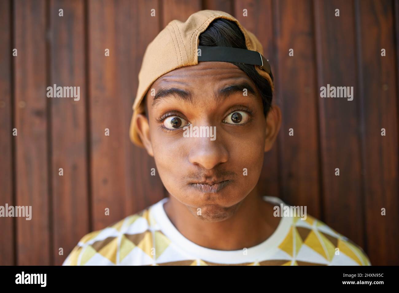 Seien Sie nie zu ernst. Porträt eines Jungen im Teenageralter, der ein Gesicht macht, während er gegen eine Holzwand steht. Stockfoto