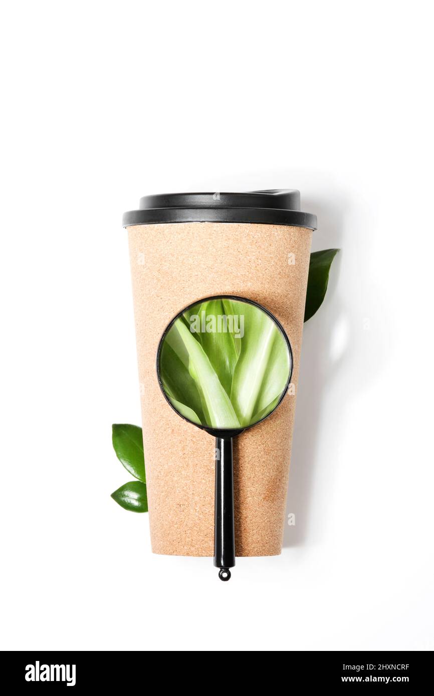 Lupe zeigt Pflanze auf wiederverwendbarem Öko-Kaffee oder Teetasse auf weißem Hintergrund. Nachhaltiger Lebensstil.Umweltfreundlich. Bewusster Konsum Stockfoto