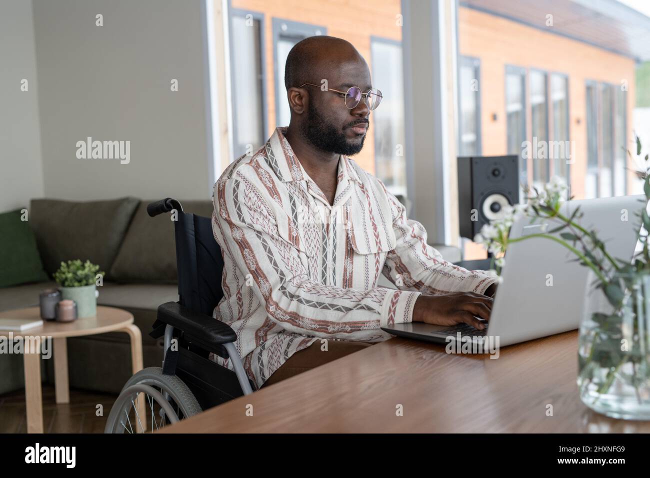 Junge, moderne Angestellte oder Freiberufler, die vor dem Laptop arbeiten, während sie am Tisch im Wohnzimmer der geräumigen Wohnung sitzen Stockfoto