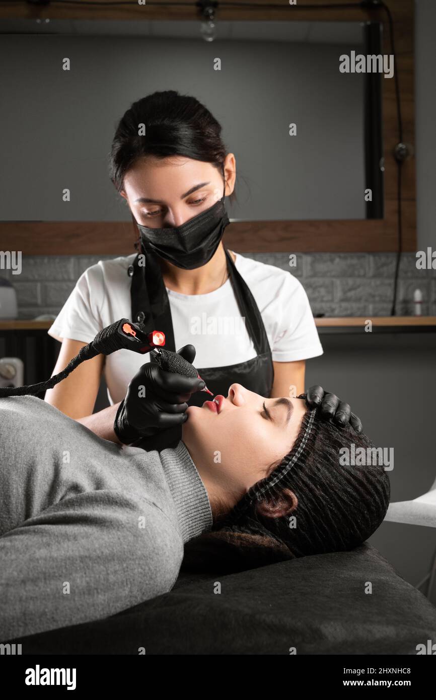 Dauerhaftes Make-up. Spa Schönheitsbehandlungen. Junge Frau. Der Meister legt das Tattoo auf die Lippen. Professionelle Microblading im Gesicht. Weibliche Kosmetologie Stockfoto