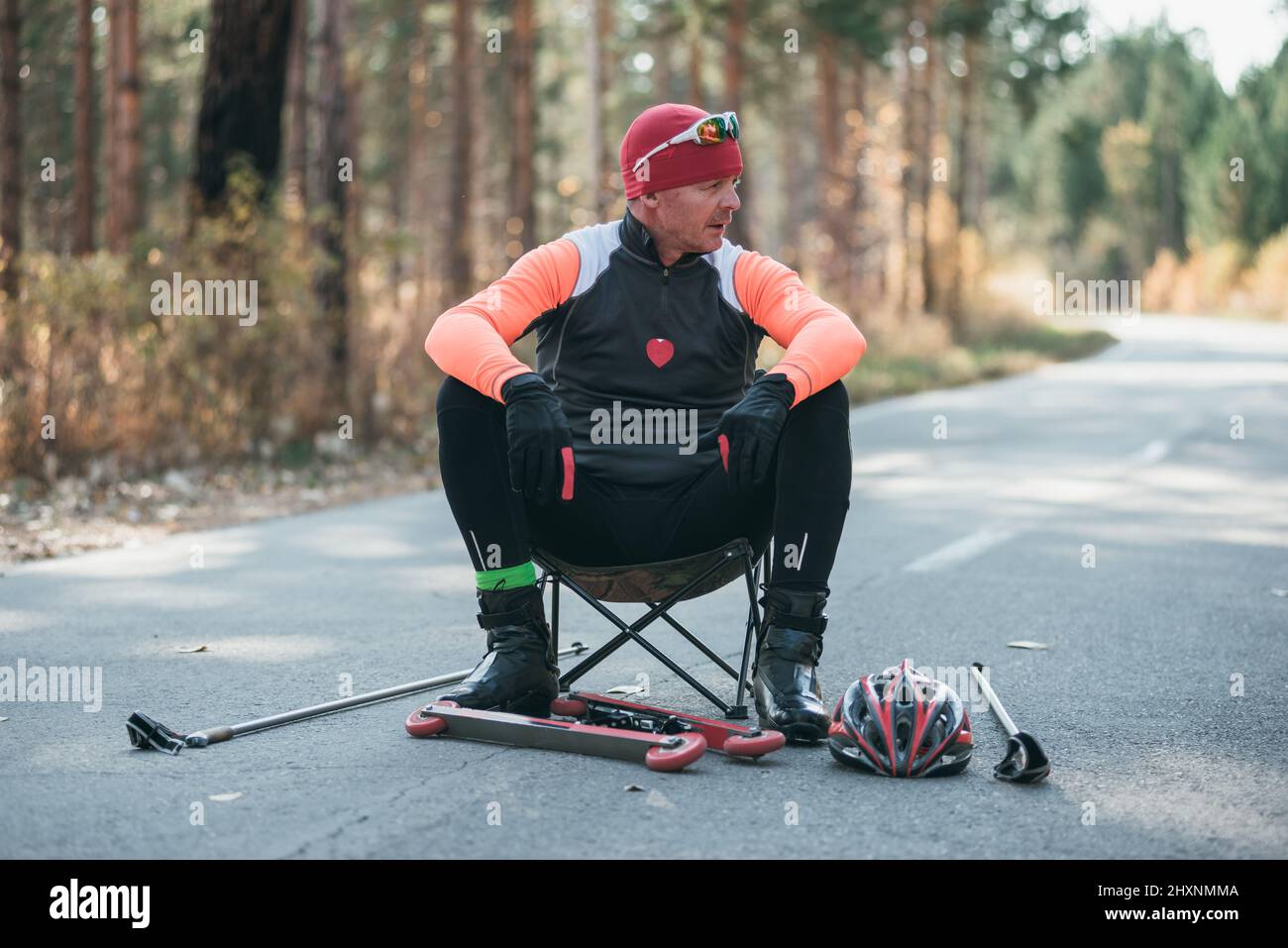 Training eines Athleten auf den Rollern. Biathlon-Fahrt auf den Rollskiern mit Skistöcken, im Helm. Herbsttraining. Rollensport. Erwachsener Mann, der auf Schlittschuhe reitet. Der Athlet bereitet sich auf den Start vor. Stockfoto