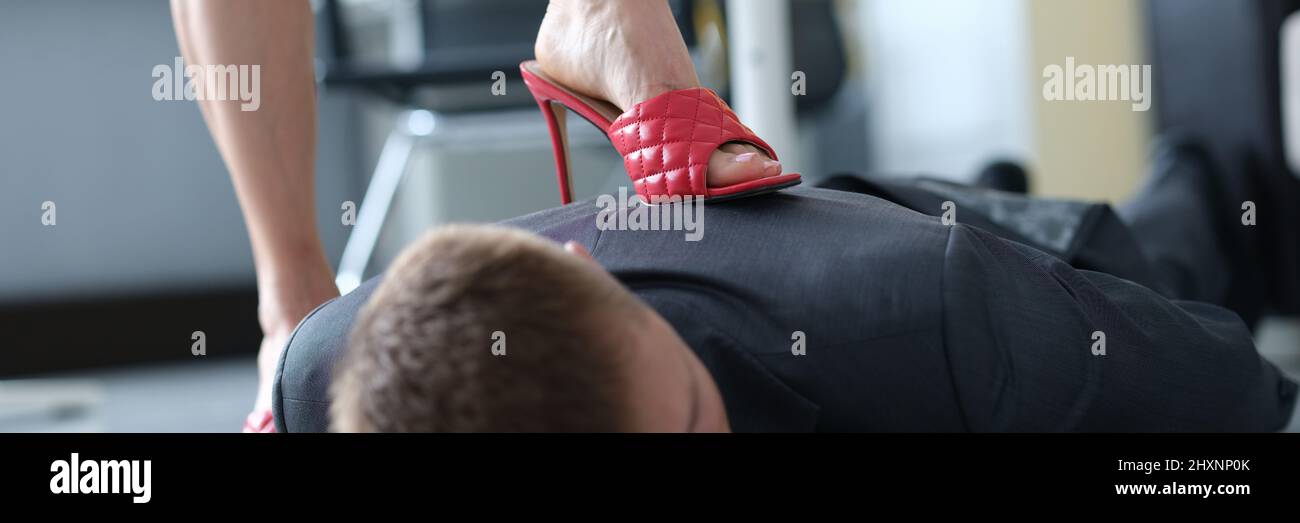 Frau in roten Sandalen mit Absätzen steht auf dem Rücken eines lügenden Mannes Stockfoto