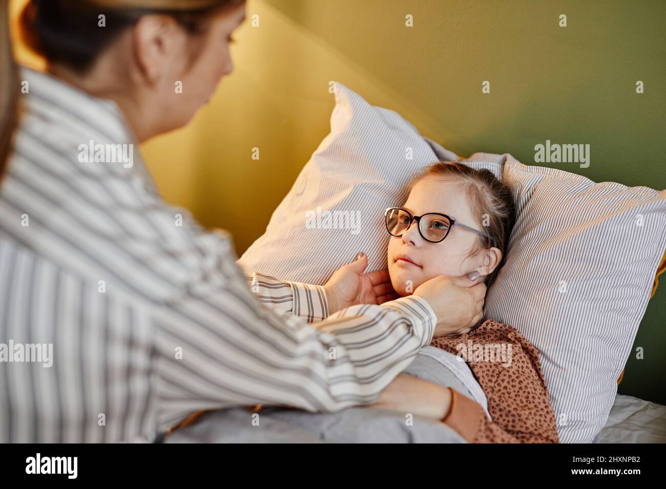 Porträt einer fürsorglichen Mutter, die während der Schlafenszeit ein Kind mit Down-Syndrom zupft, Raum kopieren Stockfoto