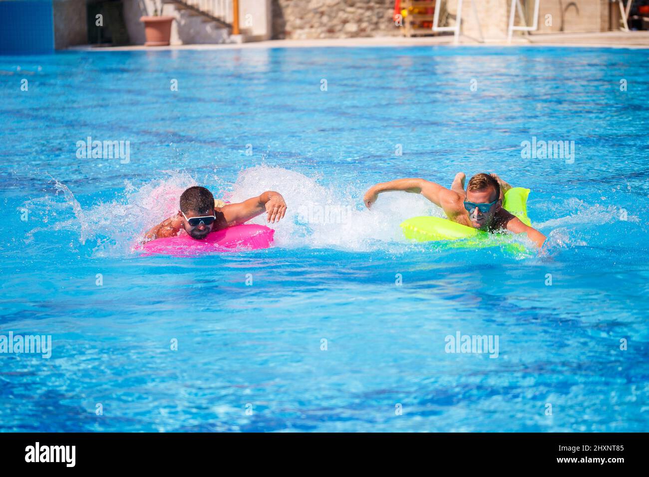 Zwei Männer schwimmen im Pool und schweben auf aufblasbaren Matratzen und entspannen sich Stockfoto