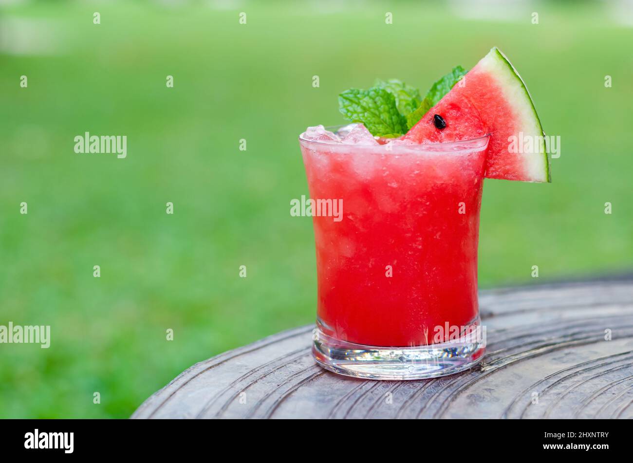 Ein Glas Wassermelone-Smoothie wird für das Sommergetränk-Konzept auf einen Tisch mit verschwommenem grünem Gartenhintergrund gestellt. Stockfoto