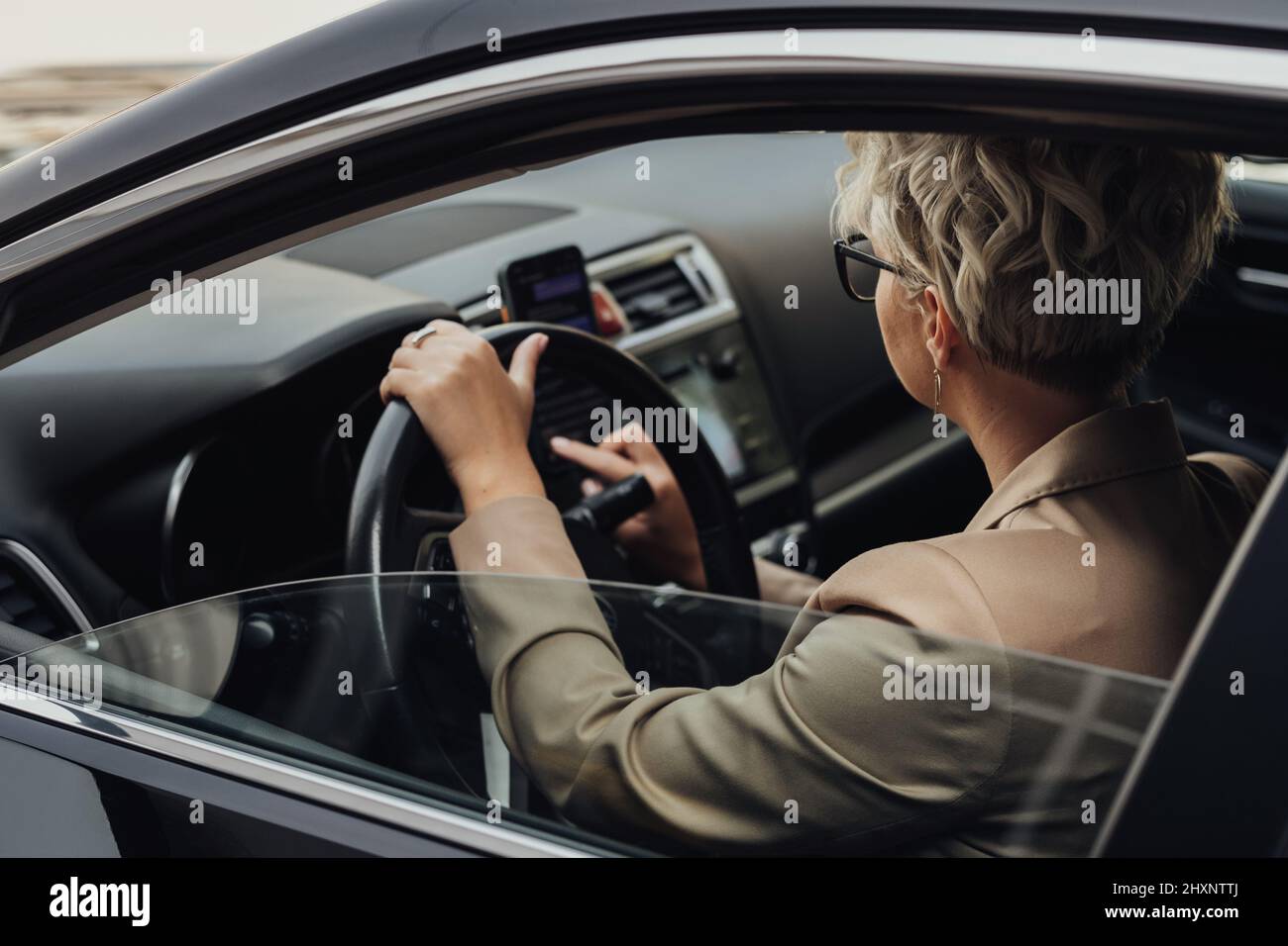 Geschäftsfrau, die während der Fahrt mit dem Auto ein Smartphone benutzt, Blick vom Seitenfenster Stockfoto