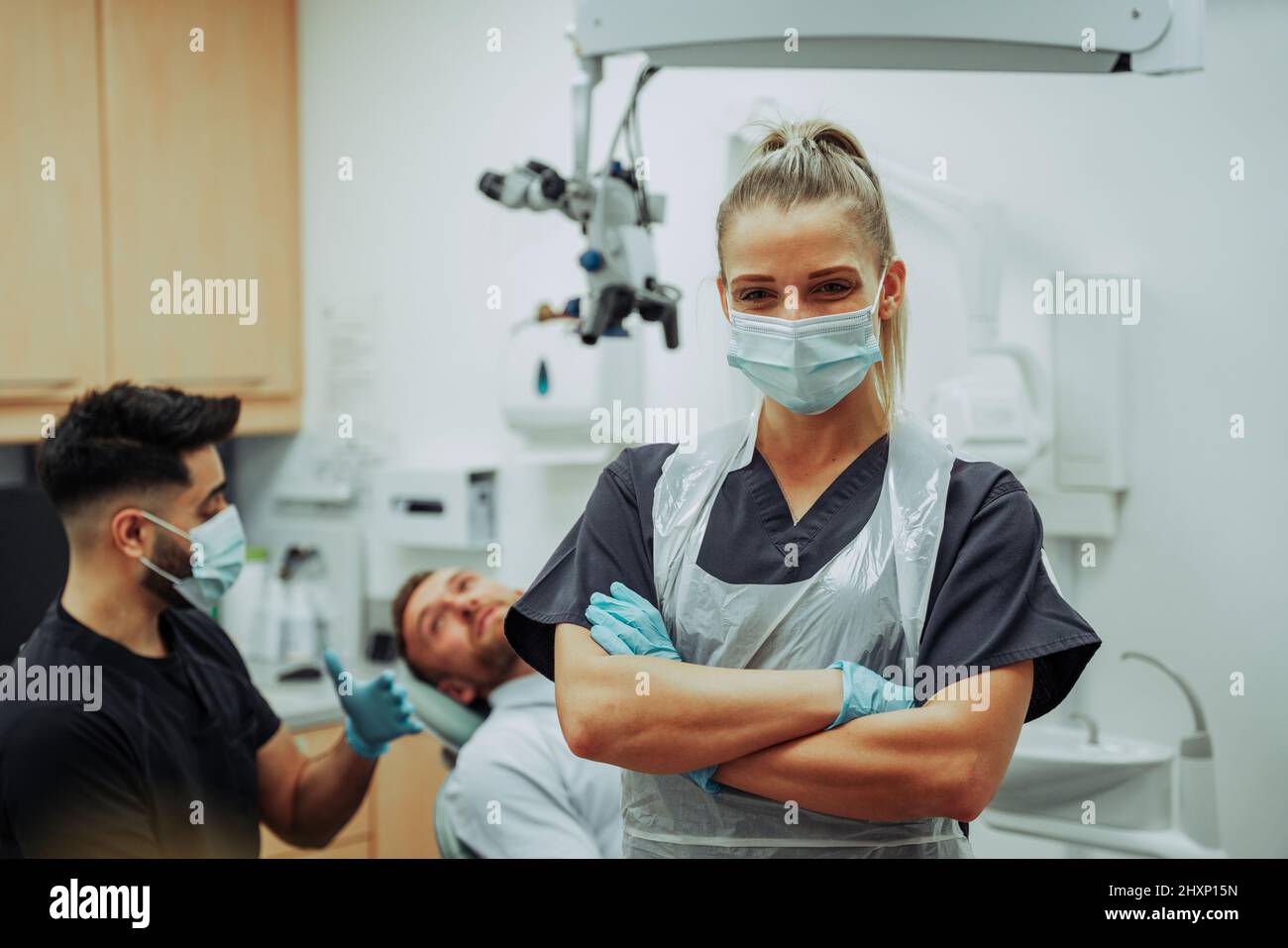 Kaukasische weibliche Zahnärztin, die eine chirurgische Maske trägt, die mit gekreuzten Armen im Ärztezimmer steht Stockfoto