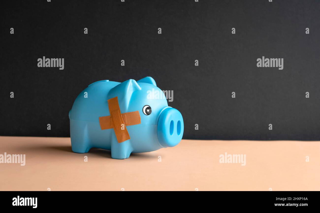 Kaputtes Sparschwein mit Band-Verbandszeug auf dem Tisch. Pleite, bankrotte oder Rezession Konzept. Stockfoto