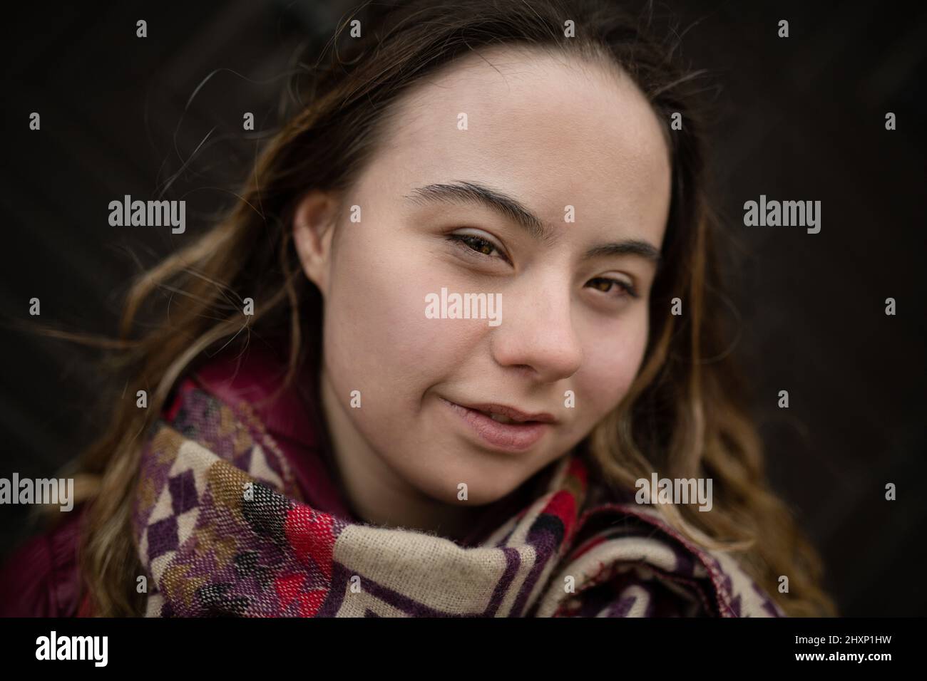 Nahaufnahme einer jungen Frau mit Down-Syndrom, die die Kamera auf schwarzem Hintergrund anschaut Stockfoto