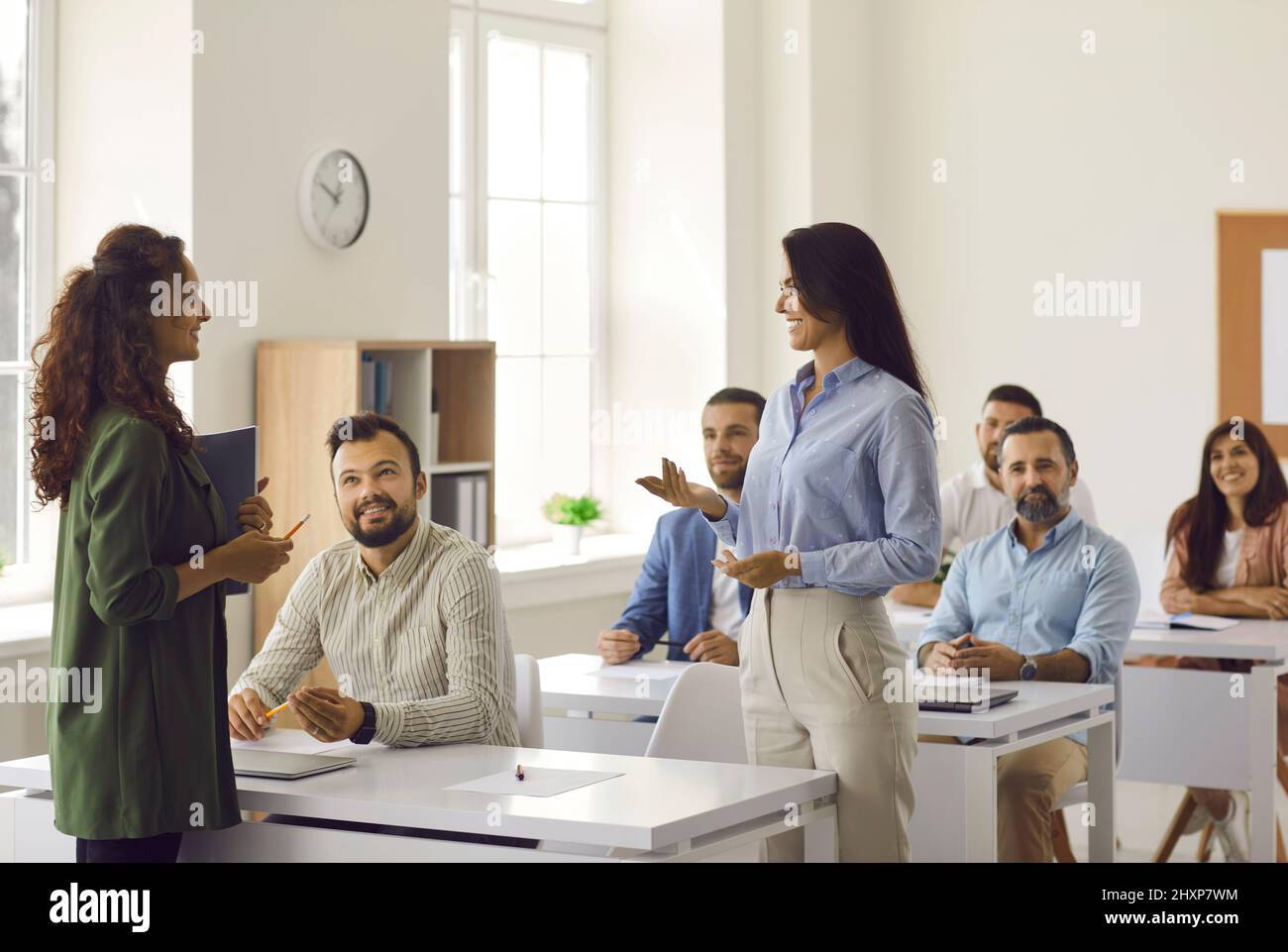 Frau im Gespräch mit Business Coach, während andere Studenten an Schreibtischen sitzen und zuhören Stockfoto