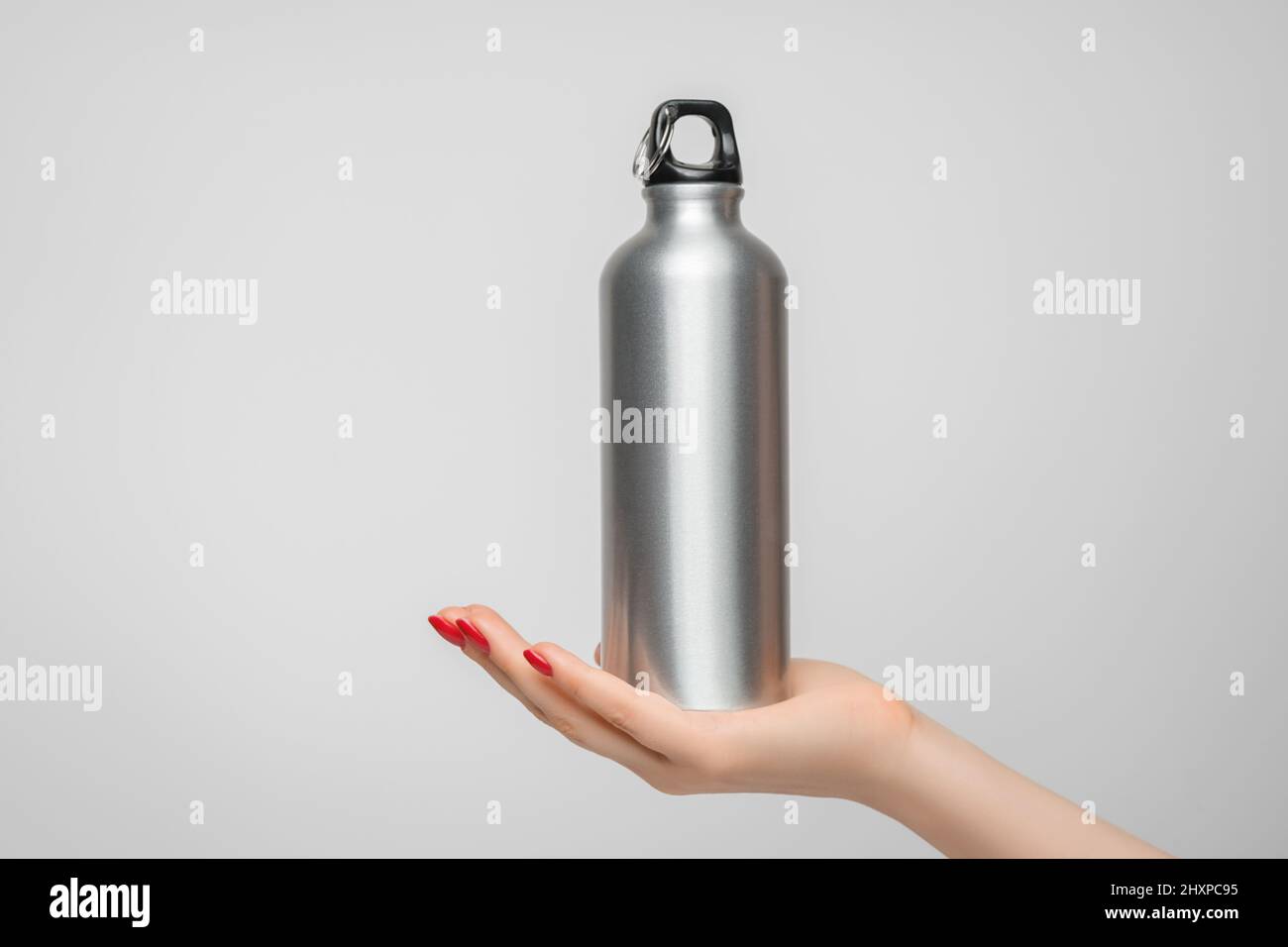 Wiederverwendbare Edelstahl-Wasserflasche in der Hand einer Frau, roter Nagellack Stockfoto