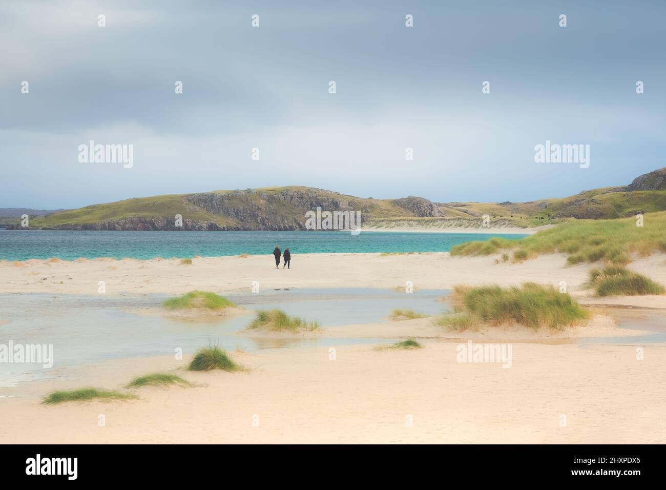 Ein entferntes Paar schlendert gemütlich am weißen Sandstrand und den grasbewachsenen Dünen am Reef Beach auf der Isle of Lewis und Harris in der Äußeren Hebd Stockfoto