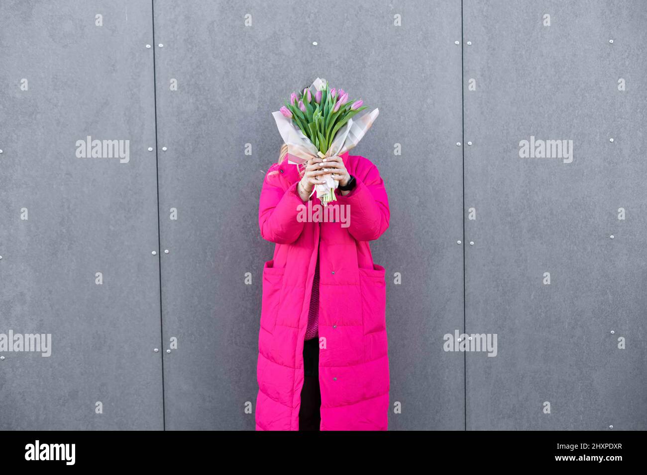 Porträt einer Frau, die sich in der Nähe der Metallwand aufhält und einen rosa violetten Blumenstrauß mit Tulpenblüten hält. Valentinstag, Frauentag Stockfoto