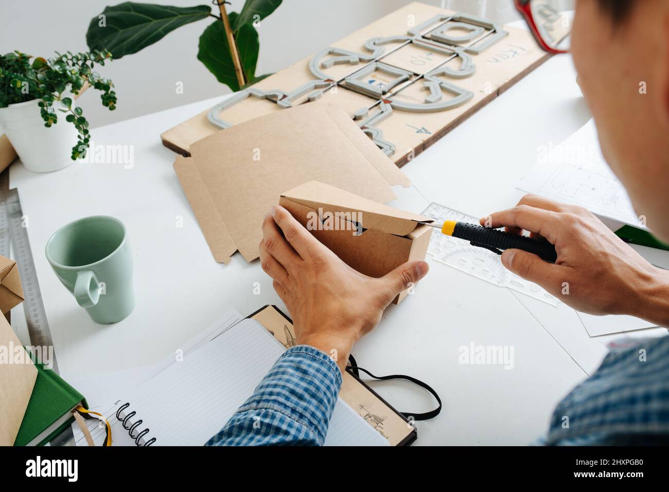 Hart arbeitend Designer Checkbox Prototyp mit einem Papierschneider. Hinter dem Schreibtisch sitzen. Stockfoto