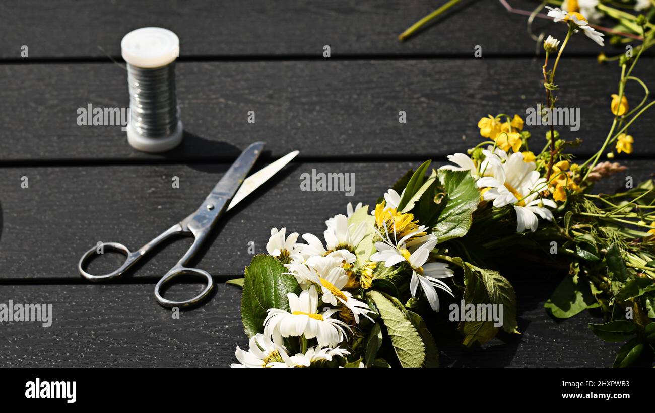 Eine schöne Blumenkrone oder einen Blumenkranz mit Draht, Schere und wilden Blumen machen. Foto aufgenommen am Mittsommerabend, einem Urlaub in Schweden. Stockfoto
