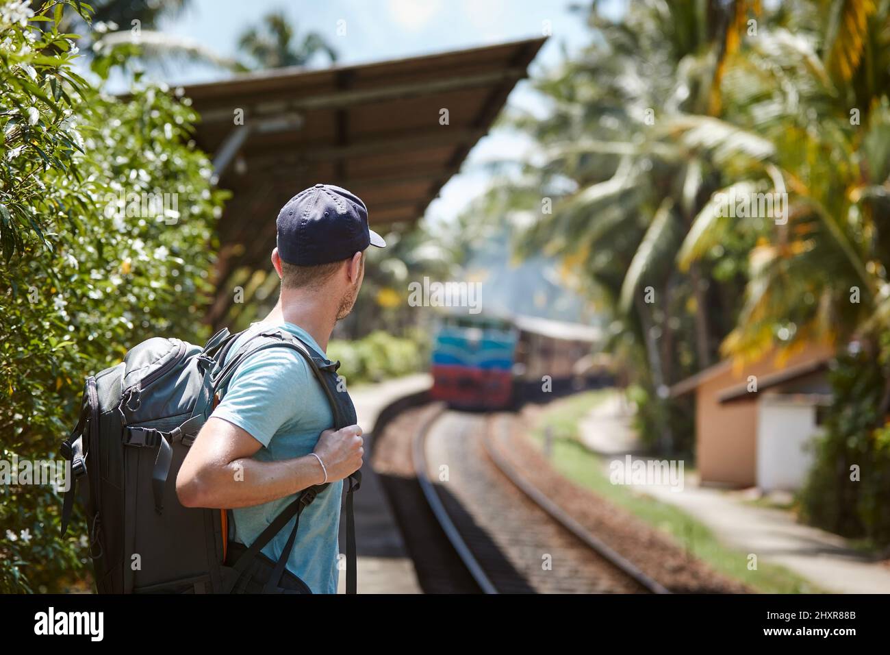 Eisenbahn in Sri Lanka. Tourist mit Rucksack wartet auf Bahnsteig und schaut auf ankommenden Zug. Stockfoto