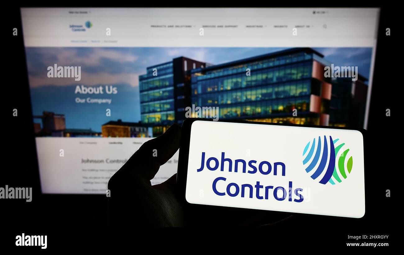 Person mit Mobiltelefon und Logo der Firma Johnson Controls International plc (JCI) auf dem Bildschirm vor der Webseite. Konzentrieren Sie sich auf die Telefonanzeige. Stockfoto