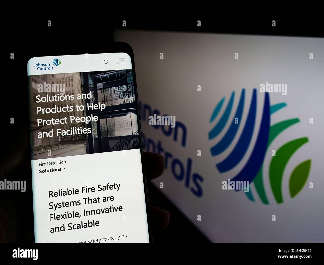 Person mit Mobiltelefon und Webseite der Firma Johnson Controls International plc (JCI) auf dem Bildschirm mit Logo. Konzentrieren Sie sich auf die Mitte des Telefondisplays. Stockfoto