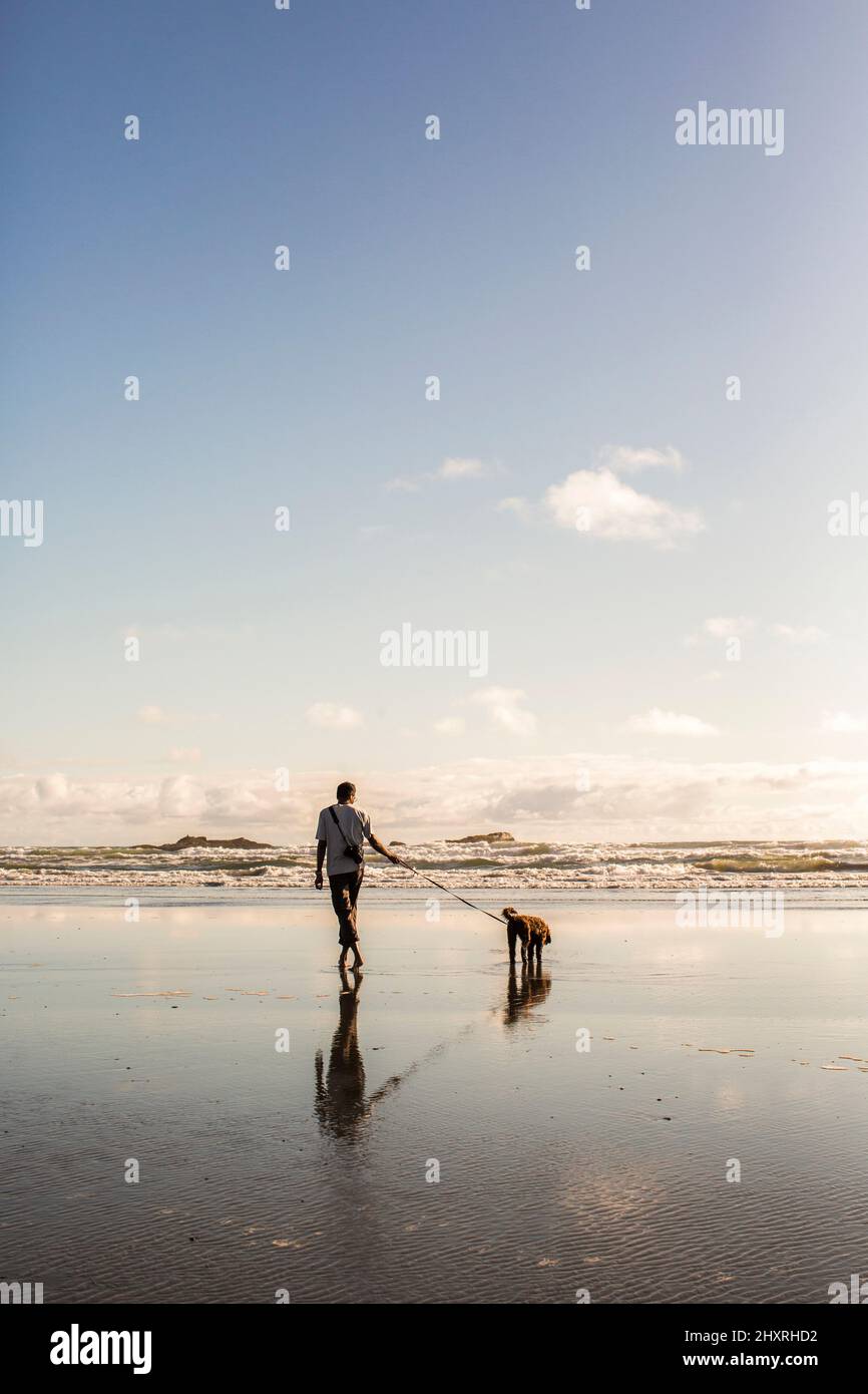Ein Mann geht mit Hund an der Leine in einer hellen Strandszene Stockfoto