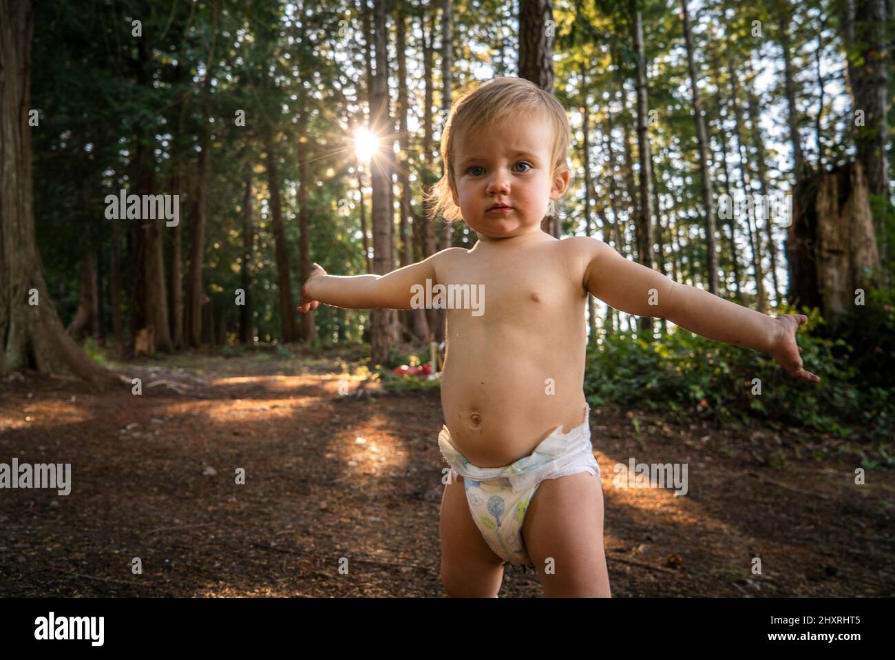 Baby in Windel steht mit ausgestreckten Armen im Wald Stockfoto