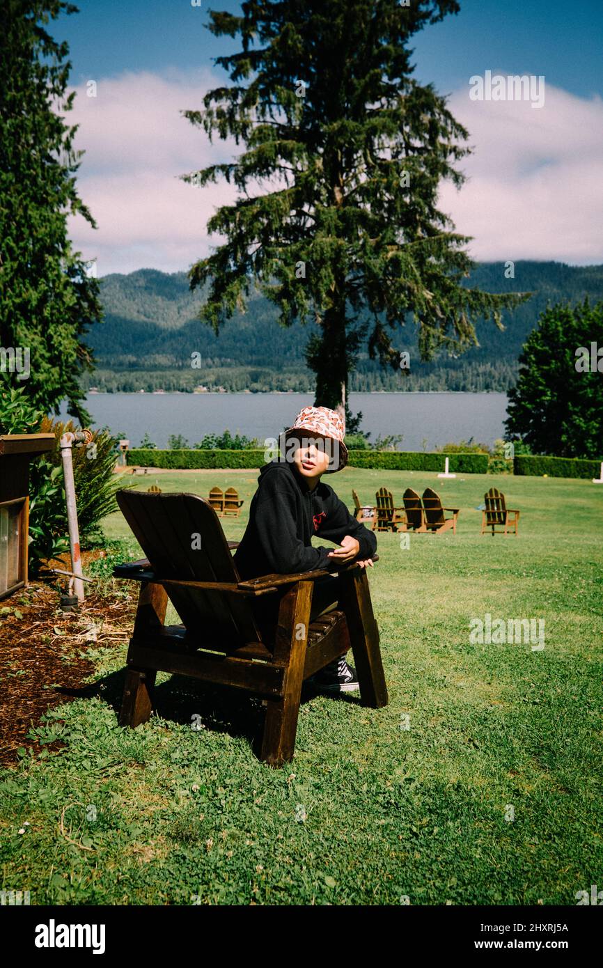 Teen Boy schaut über sollte von Adirondack Stuhl neben See Stockfoto