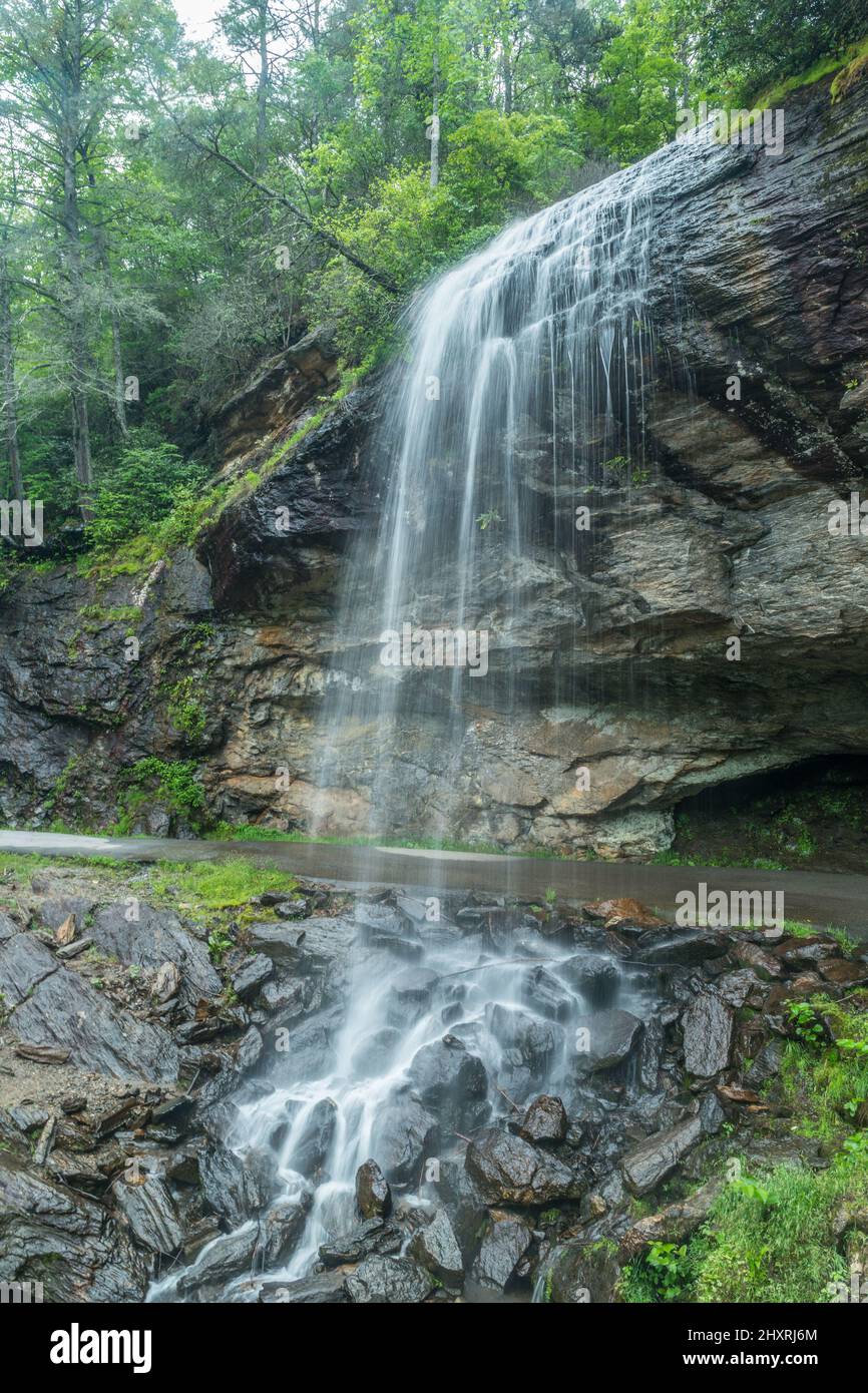 Ein Wasserfall am Straßenrand, der über eine Klippe und über eine nun geschlossene Straße führt, die Sie hinter den Wasserfällen, die zu den Felsbrocken hinunterstürzen und Ro gehen können Stockfoto