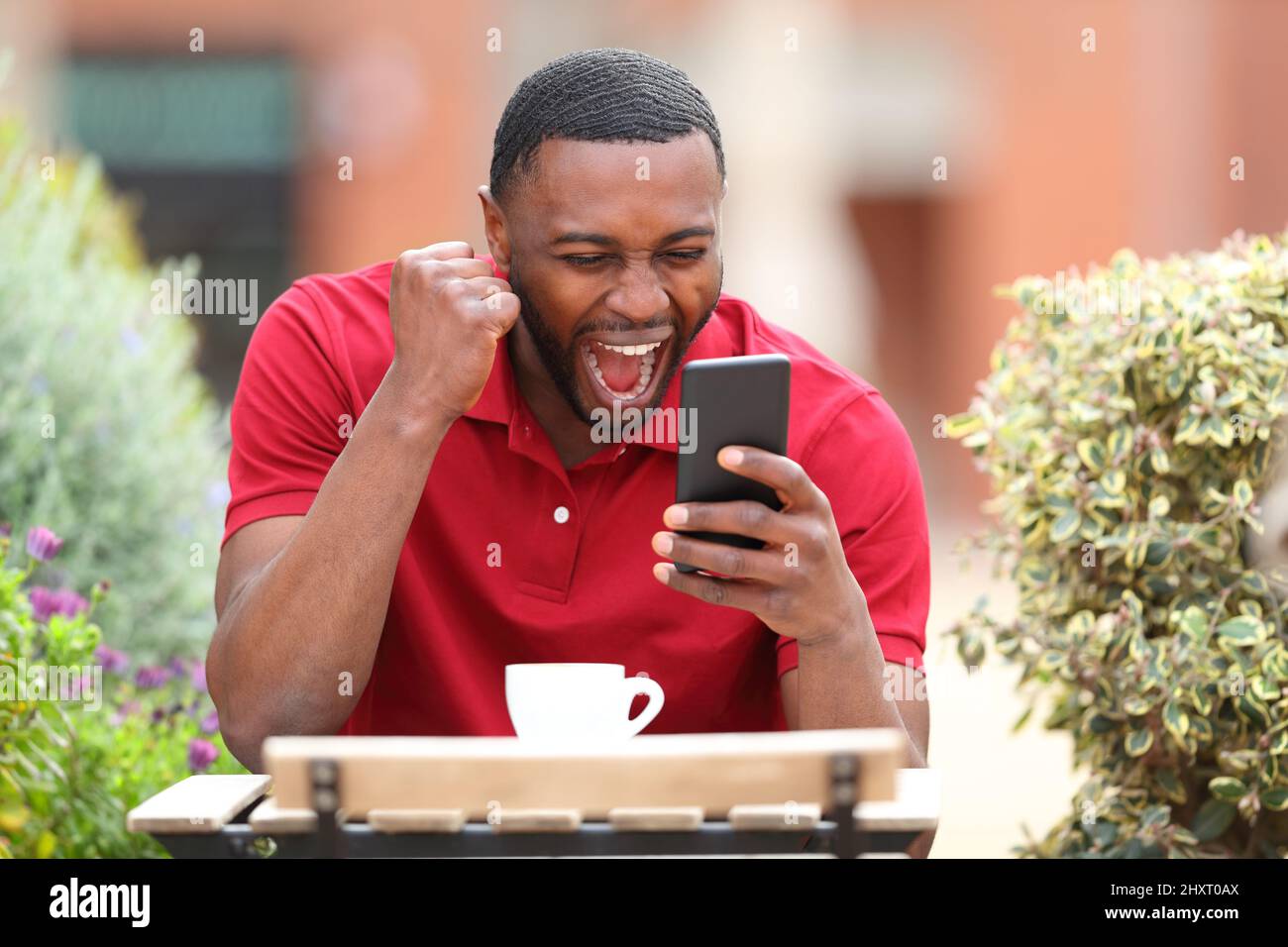 Aufgeregter Mann mit schwarzem Hautcheck-Handy feiert auf einer Barterrasse Stockfoto