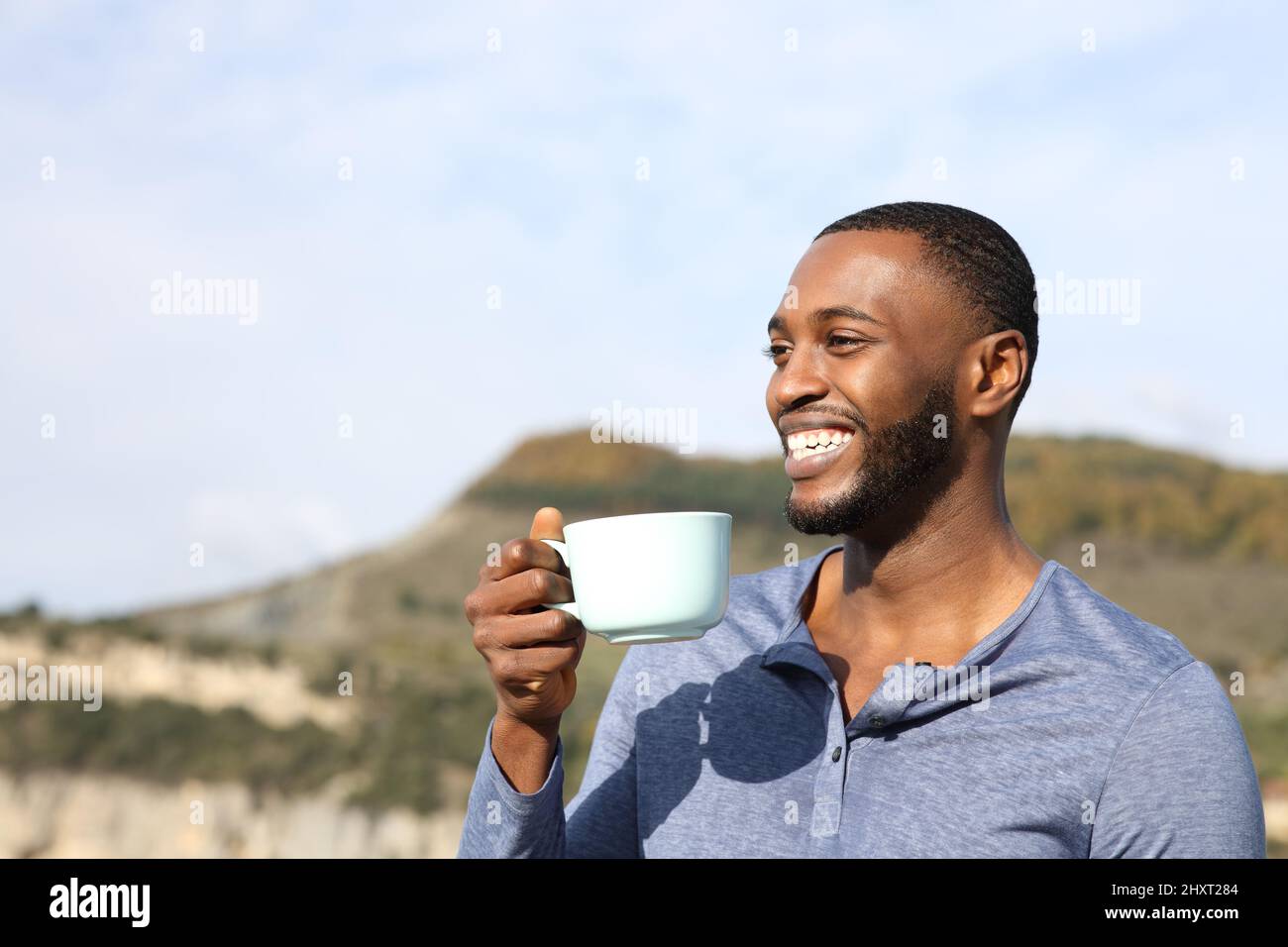 Glücklicher Mann mit schwarzer Haut lachend und trinkend Kaffee in den Bergen kontemplierend Ansichten Stockfoto