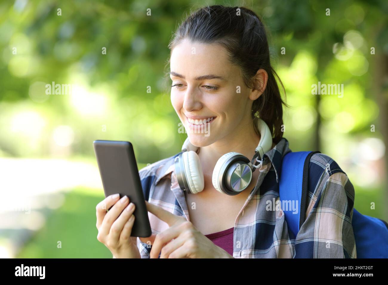 Glücklicher Student, der Smartphone benutzt, der in einem grünen Park oder auf dem Campus läuft Stockfoto