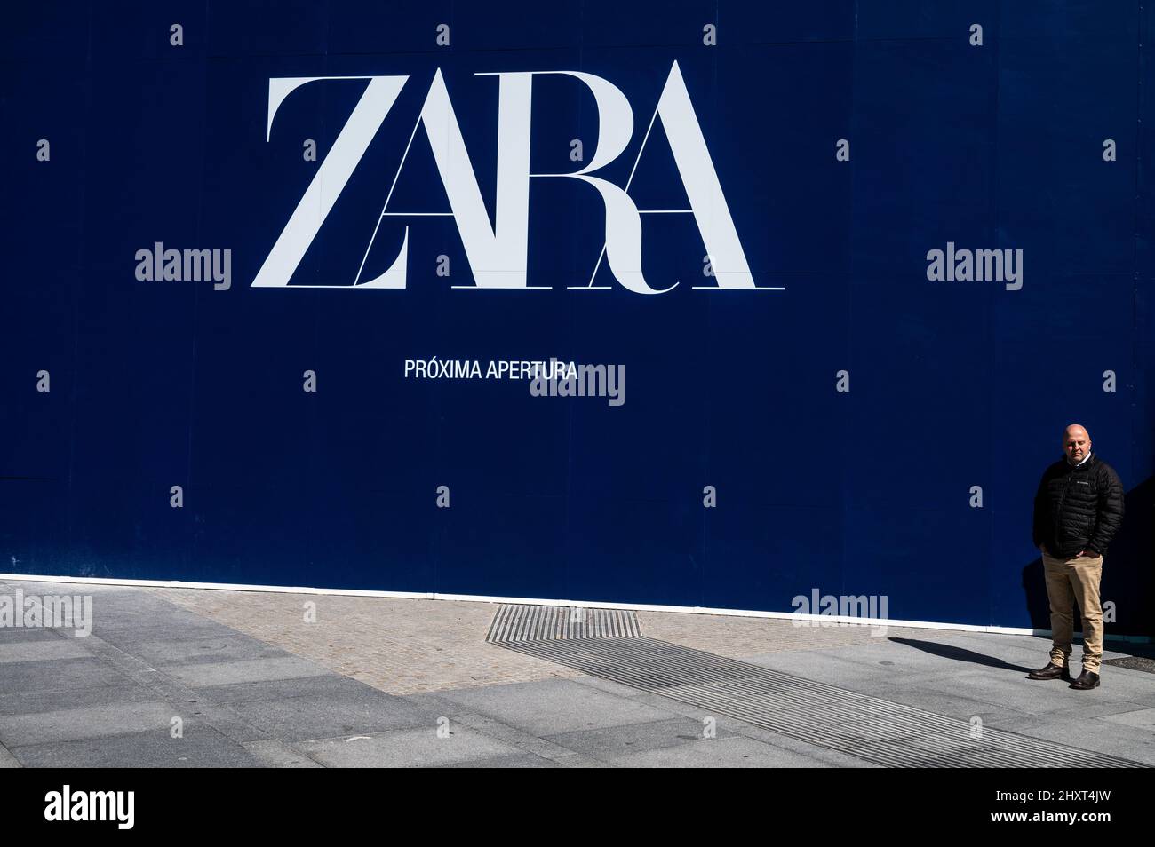 Ein Mann steht neben einer Werbung für die bevorstehende Eröffnung eines Zara-Ladens. Die Geschäfte von Zara gehören zur Inditex-Gruppe, die sich im Besitz von Amancio Ortega befindet. Stockfoto