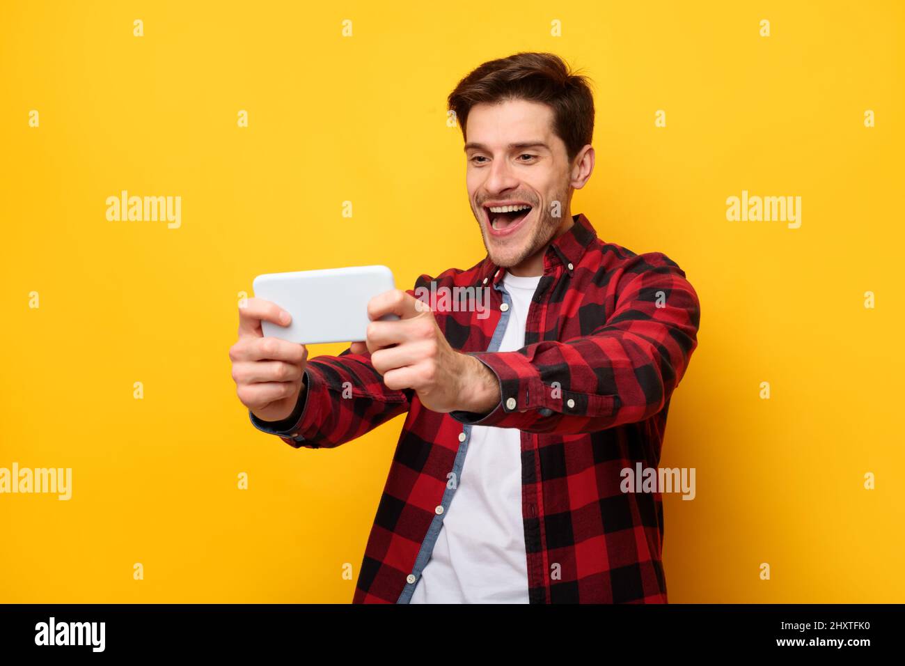 Aufgeregt Mann spielen mobile Spiele auf gelbem Hintergrund Stockfoto