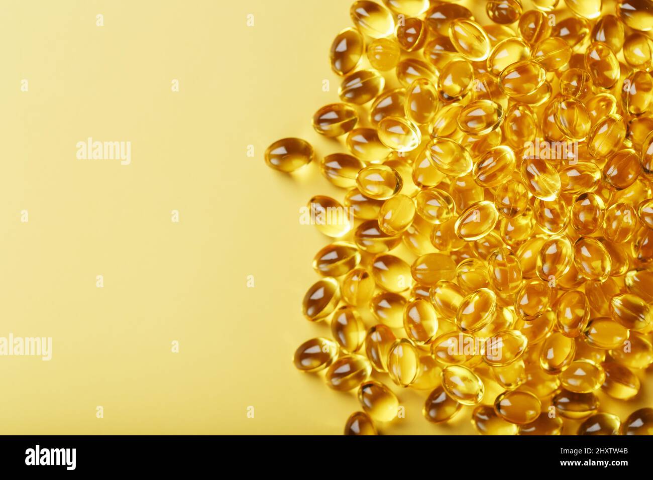 Haufen goldener Kapseln von Vitamin D3 auf gelbem Hintergrund mit freiem Platz. Biologisch aktive Substanzen der Calciferol-Gruppe sind fettlöslich o Stockfoto