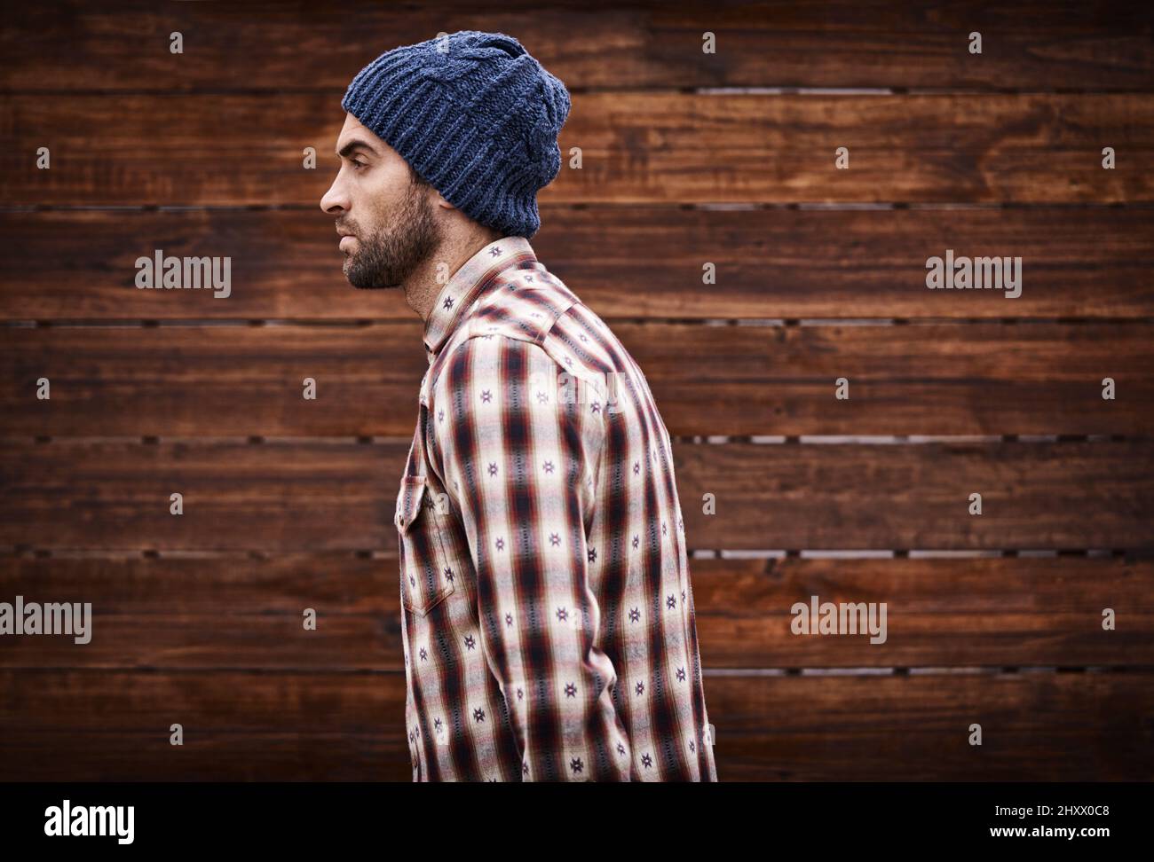Stil für die Straße. Aufnahme eines hübschen jungen Mannes in angesagter Winterkleidung vor einem hölzernen Hintergrund. Stockfoto
