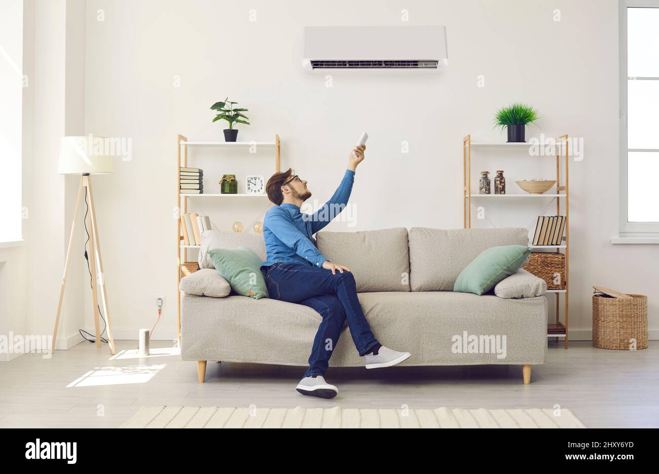 Der Mann, der zu Hause auf der Couch sitzt, schaltet die Klimaanlage per Fernbedienung Stockfoto