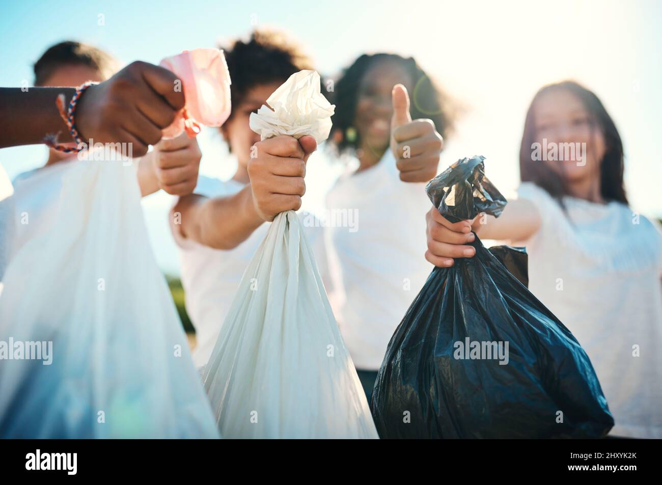 Meldung für Reinigungsarbeiten. Aufnahme einer Gruppe von Teenagern, die auf einem Feld Müll aufsammeln und im Sommercamp Daumen nach oben zeigen. Stockfoto