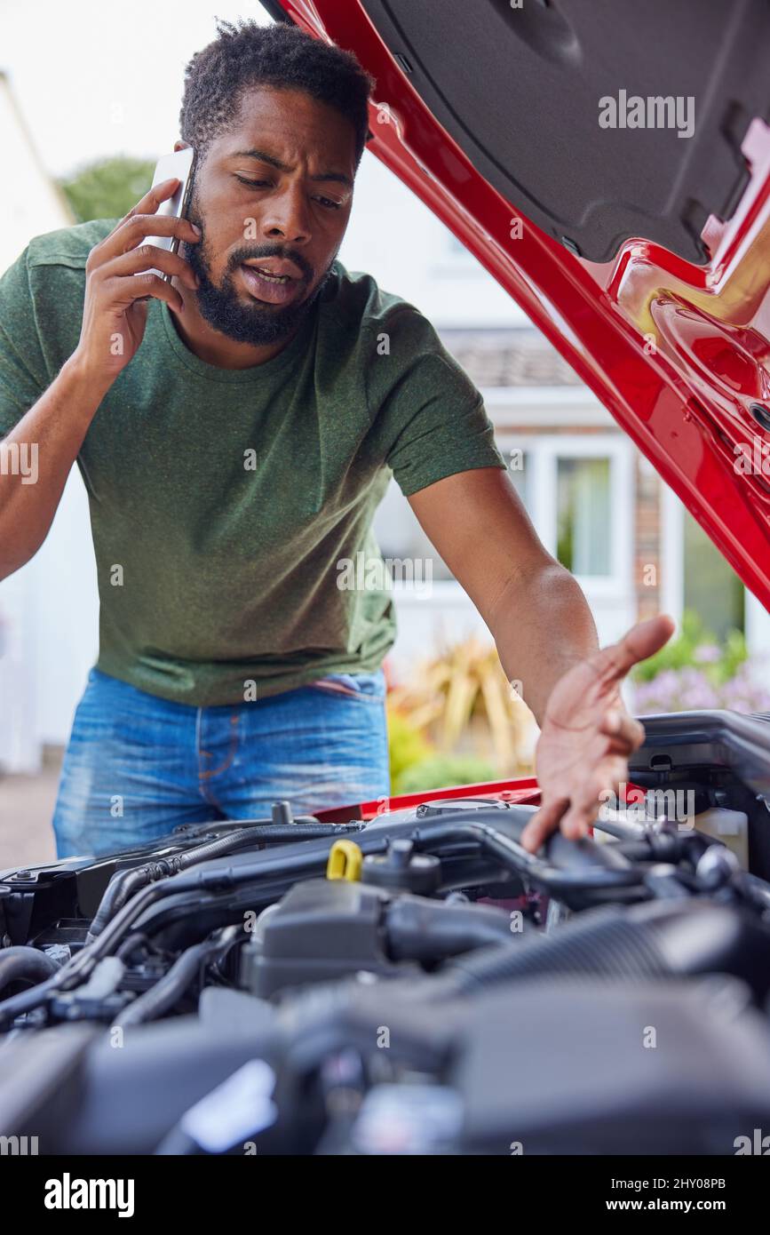 Mann, Der Den Motor Nach Einer Panne Des Autos Ansieht, Ruft Die Automatische Wiederherstellung Auf Dem Mobiltelefon An Stockfoto