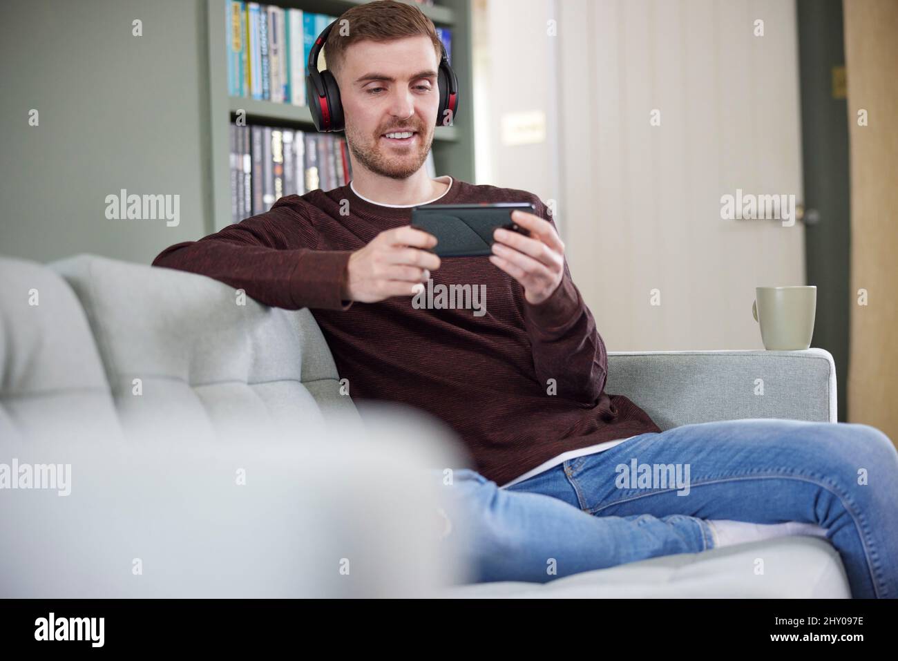 Mann Zu Hause Mit Kabellosen Kopfhörern, Der Musik Oder Film Vom Mobiltelefon Streamen Kann Stockfoto