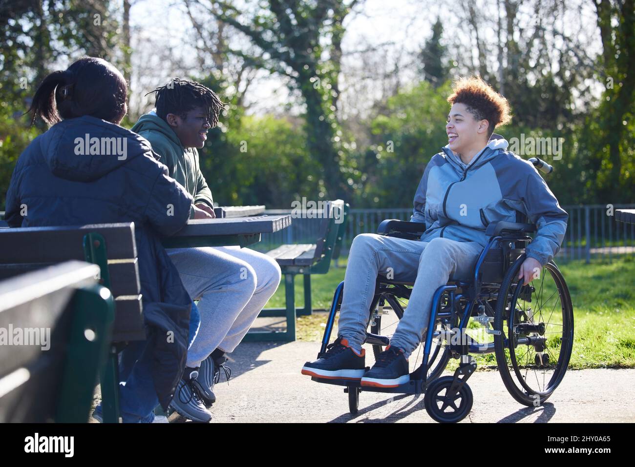 Teenage Girl In Wheelchair Aufhängen Reden Und Lachen Mit Freunden Im Park Stockfoto