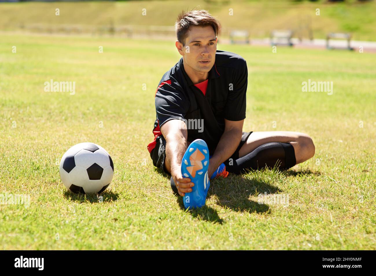Dehnen vor dem Üben. Aufnahme eines jungen Fußballers, der sich auf dem Spielfeld streckt. Stockfoto