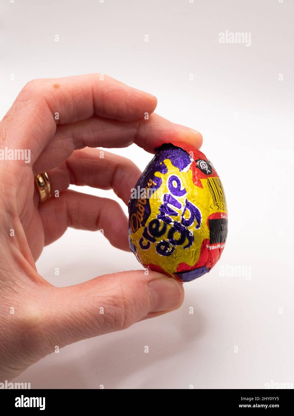 Menschliche Hand, die ein Cadbury Crème Egg vor einem schlichten weißen Hintergrund mit absichtlich selektivem Fokus hält Stockfoto