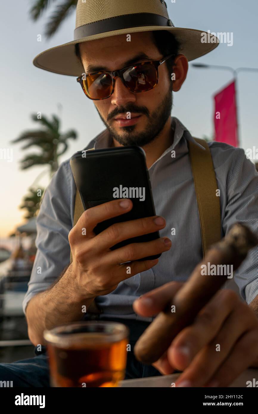 Vertikales Foto eines Hipsters an der Bar, der mit seinem Handy ein Bild zu einem teuren Rum-Schuss machte Stockfoto
