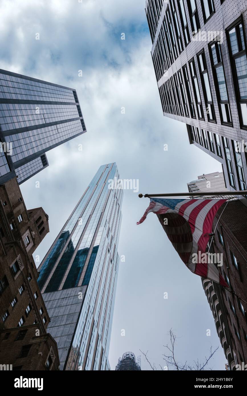 Unter den modernen Hochhäusern mit nationaler amerikanischer Flagge auf der Straße von New York City gegen den bewölkten Himmel Stockfoto